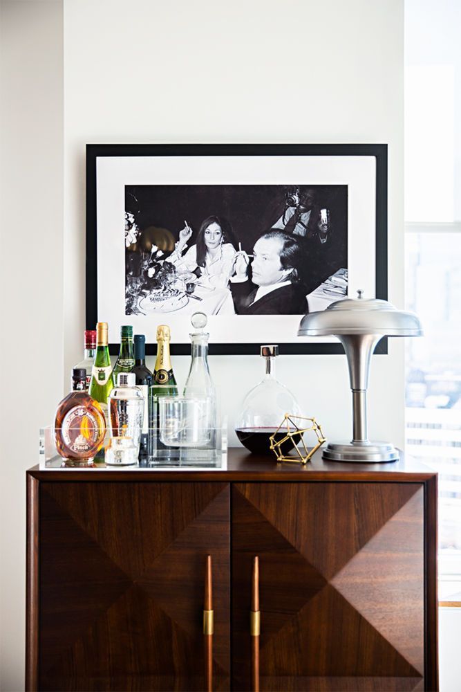 a wooden cabinet with bottles and glasses on it in front of a framed black and white photograph