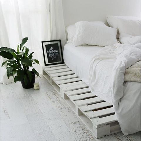 a bed made out of pallets with white sheets and pillows on it, next to a potted plant