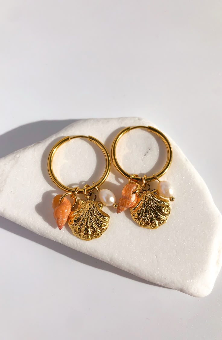 HotSummerNights  Indulge in the allure of summer nights with our captivating "Hot Summer Nights" charm hoop earrings.  Unique Design: Our earrings feature a stunning combination of a golden stainless steel clam seashell, a delicate white freshwater pearl, and a charming natural seashell charm. This unique design sets them apart from traditional earrings and adds a touch of individuality to your look. Versatile Style: Whether you're dressing up for a beach party, a romantic dinner, or a casual ou Affordable Starfish Charm Earrings For Gifts, Cheap Summer Beach Earrings, Beach Jewelry With Dangling Charms, Shell-shaped Pearl Charm Earrings As Gift, Beach Dangle Charms Jewelry, Ocean-inspired Jewelry With Dangling Charms For Gifts, Handmade Shell-shaped Hoop Earrings For Summer, Beach Pearl Charm Shell Earrings, Pearl Charm Shell Earrings Gift