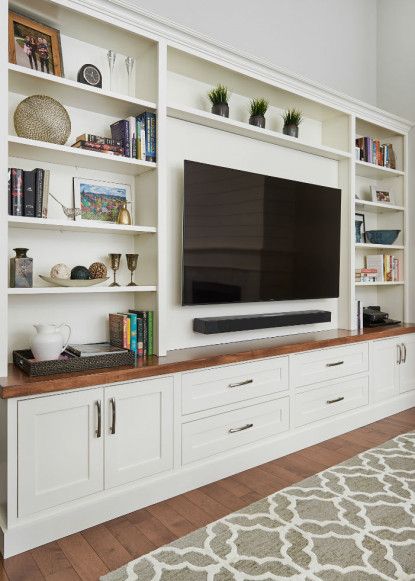 a flat screen tv sitting on top of a wooden shelf in front of white bookshelves