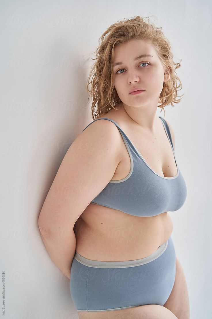 a woman in a blue bra top leaning against a white wall with her hands on her hips