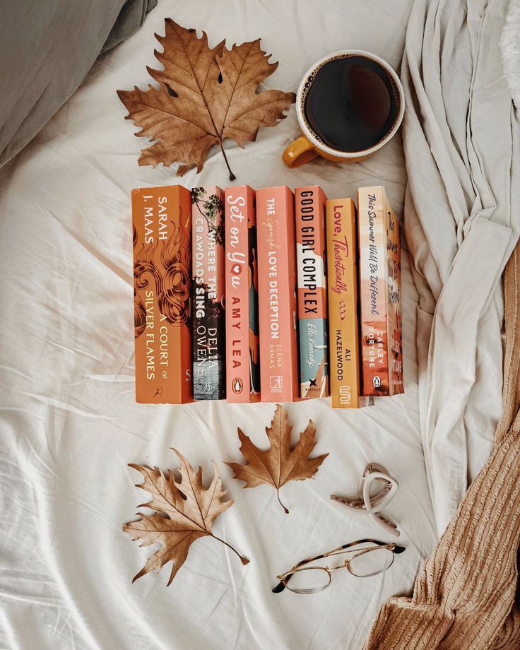 a cup of coffee sits on top of a bed next to books and autumn leaves