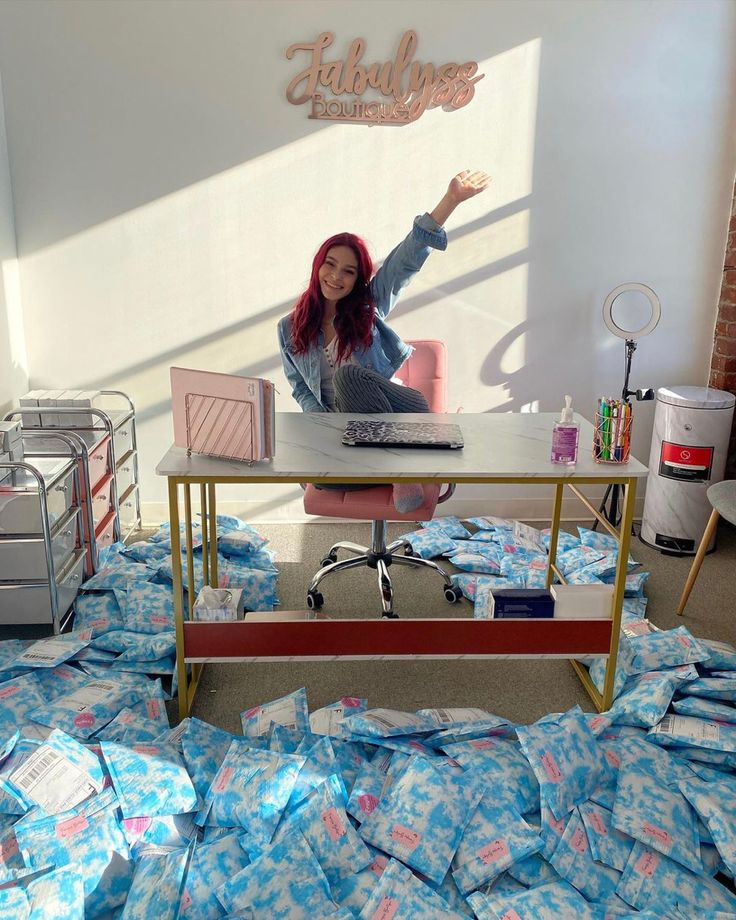 a woman sitting at a desk with her arms in the air, surrounded by blue sheets