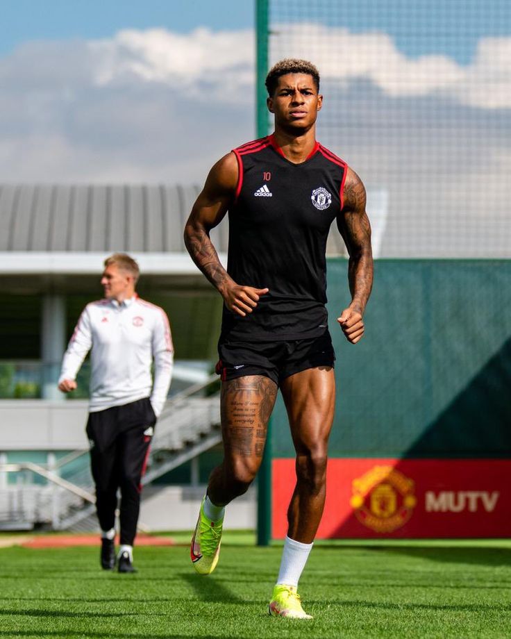 a man running on a field with another man in the background wearing black and red