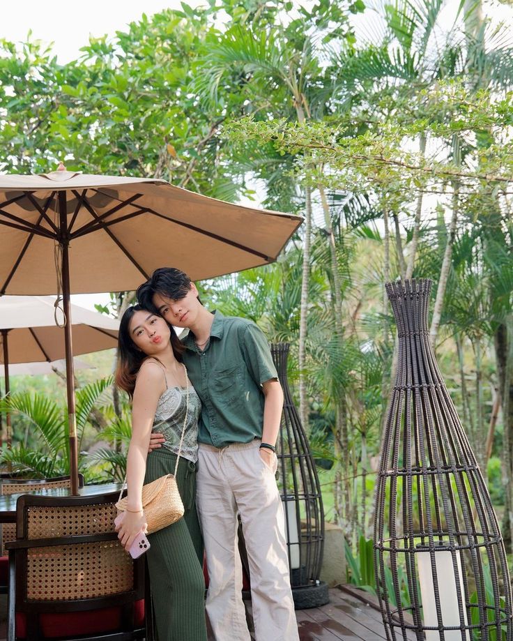 a man and woman standing next to each other in front of an umbrella on a patio