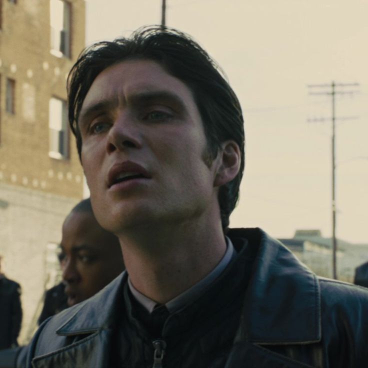 a man in a leather jacket looking off into the distance with other people behind him