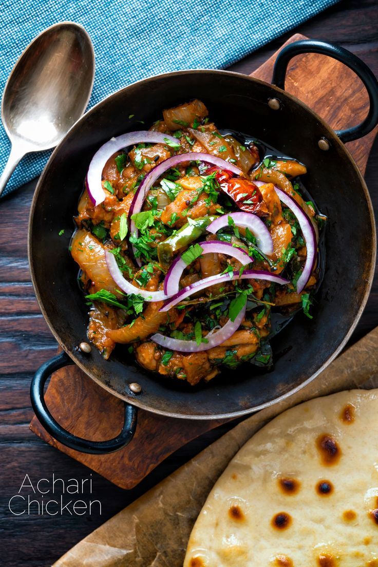 a skillet filled with chicken and onions on top of a wooden table next to pita bread