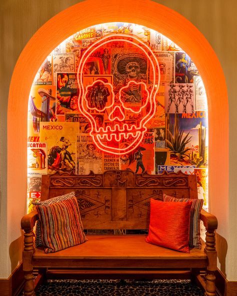 a wooden bench sitting under a neon lit skull head on the side of a wall