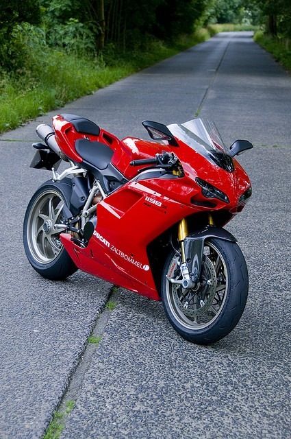 a red motorcycle parked on the side of a road next to some grass and trees