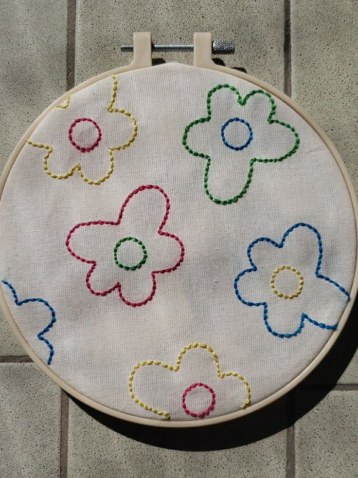 an embroidered hoop with flowers on it sitting on a tile floor next to a brick wall