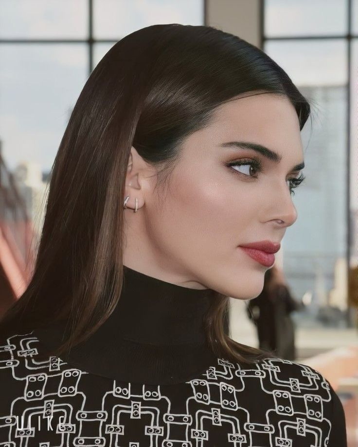 a woman with long hair wearing earrings and a black top is looking off to the side