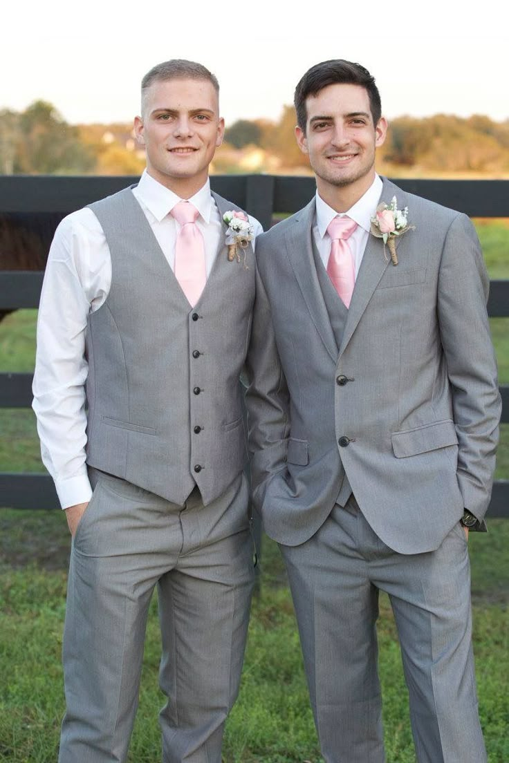 two men in suits standing next to each other on a grass covered field near a fence