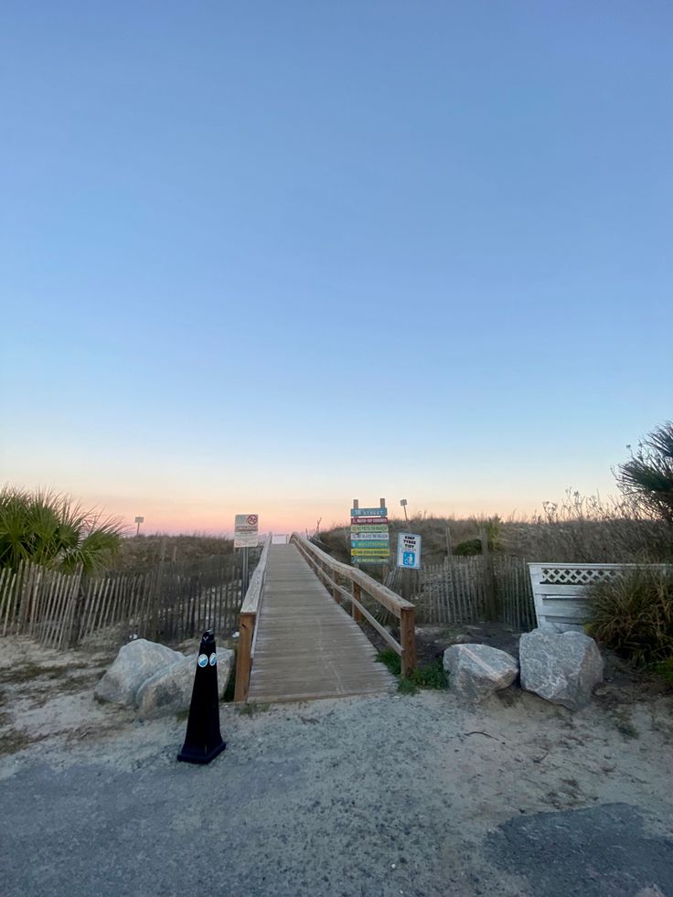 a wooden walkway leading to the beach at sunset with a sign in the foreground