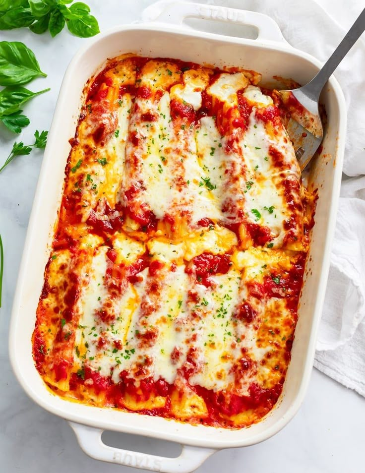 a casserole dish filled with lasagna sauce, cheese and parsley