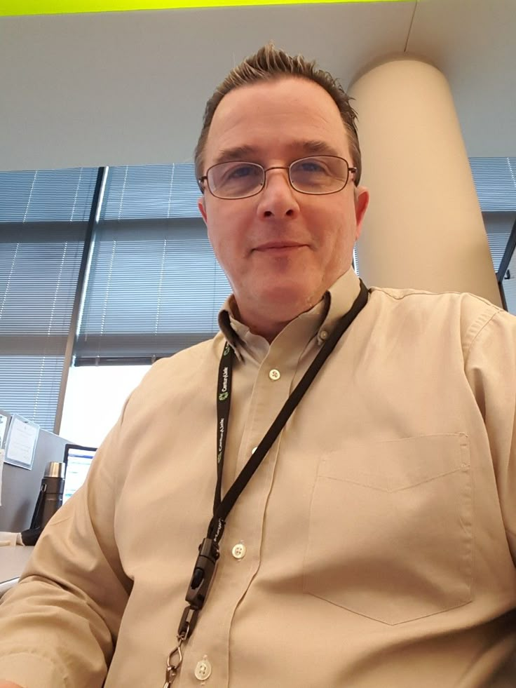 a man with glasses and a lanyard around his neck sitting in front of a window