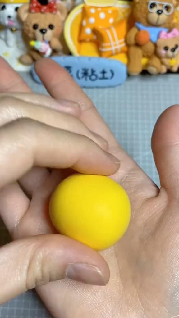 a person is holding a yellow ball in their hand and some teddy bears are on the table behind them