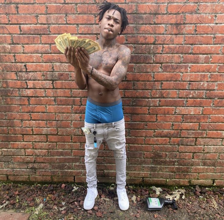 a man standing in front of a brick wall holding money