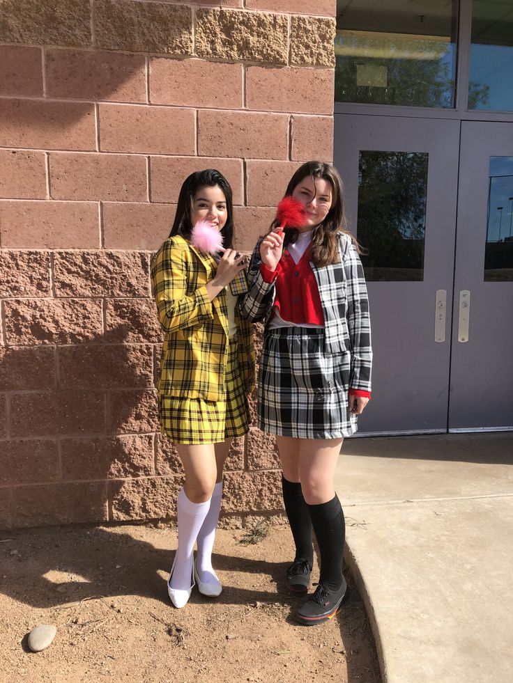 two young women standing next to each other in front of a brick building holding candy