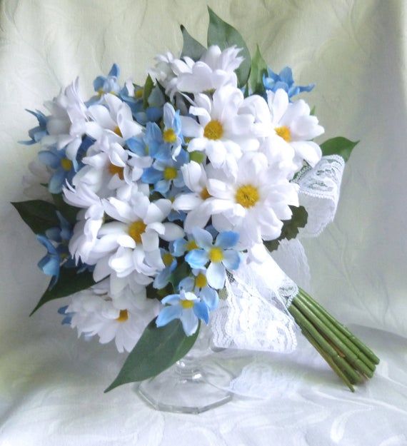 a bouquet of white and blue flowers in a glass vase on a lace tablecloth