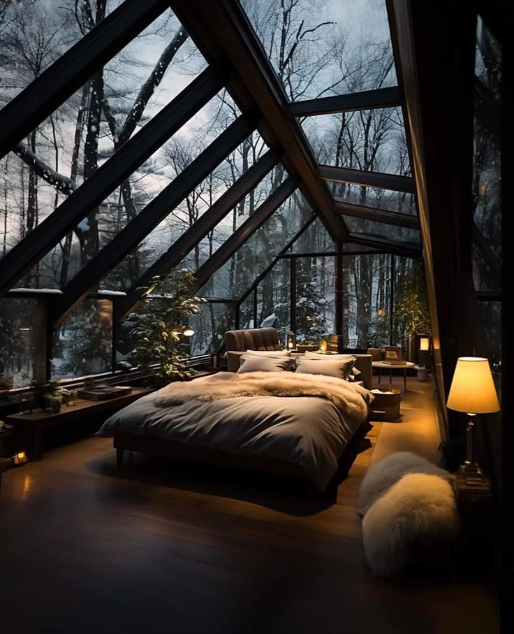 a bed sitting under a glass roof next to a window filled with snow covered trees