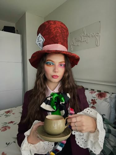 a woman wearing a red hat and holding a green teapot in front of her face