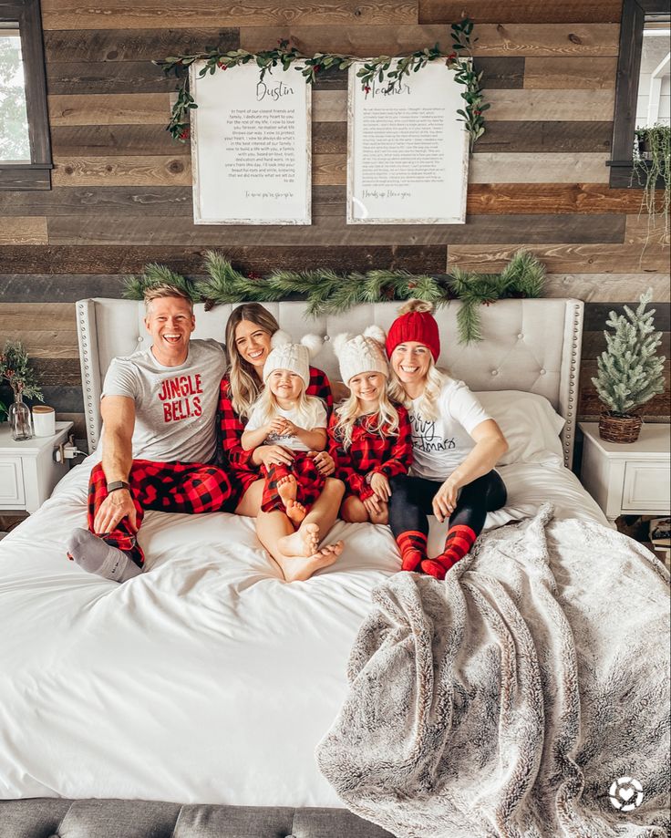 a family in matching pajamas sitting on a bed with christmas decorations and greenery around them