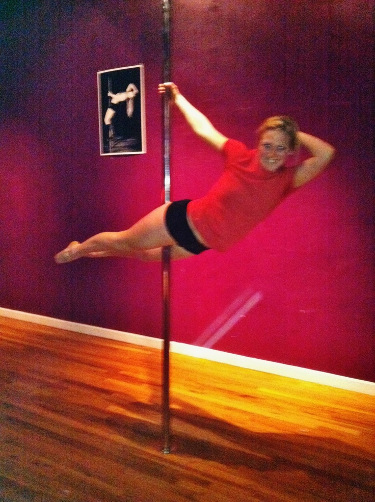 a woman in red shirt and black shorts standing on pole with one leg raised up