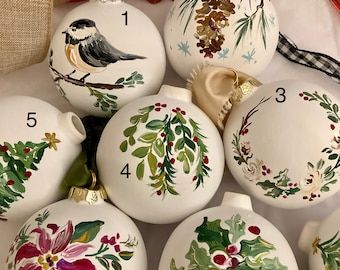 christmas baubles decorated with birds, holly and pine cones are laid out on a table