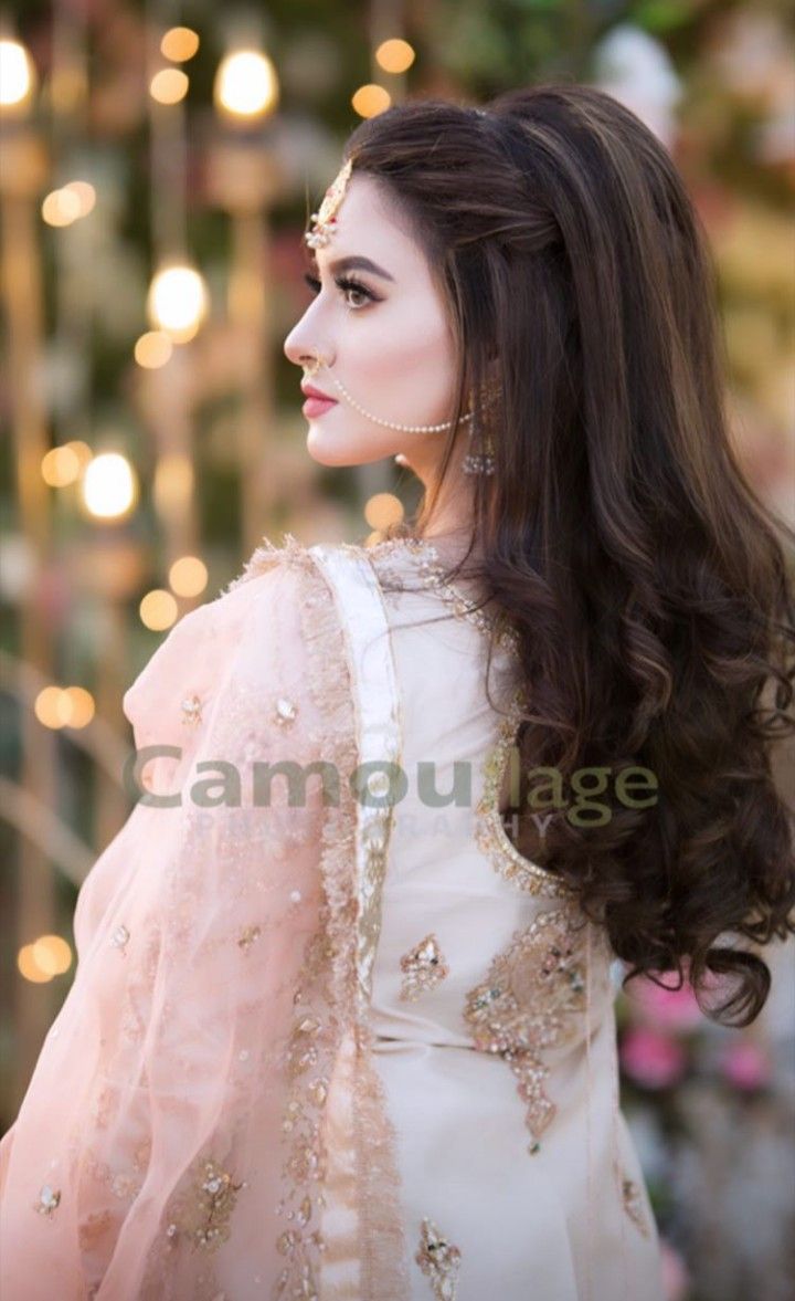 a woman with long hair wearing a white dress and gold jewelry, standing in front of lights