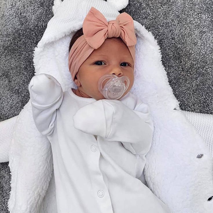 a baby wearing a pink bow laying on top of a blanket with a pacifier in it's mouth