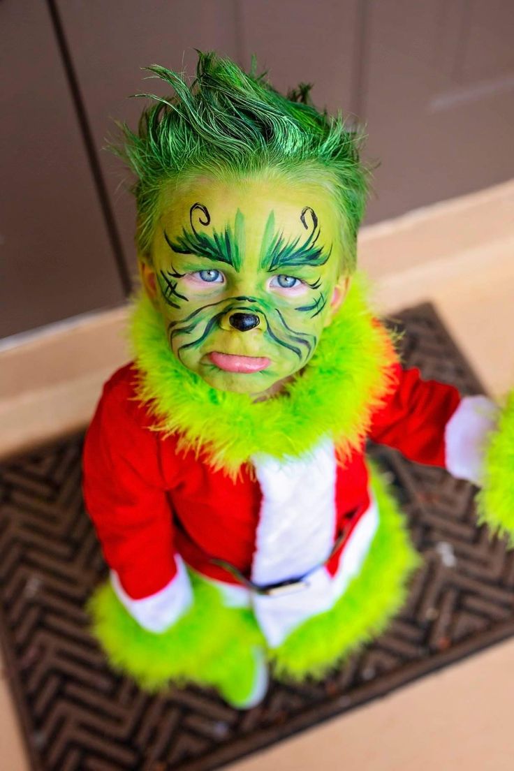 a young child with green hair and face paint is sitting on the floor wearing a costume