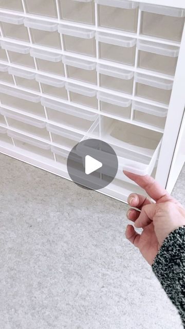 a person is pointing at the bottom of a book shelf with white bins on it