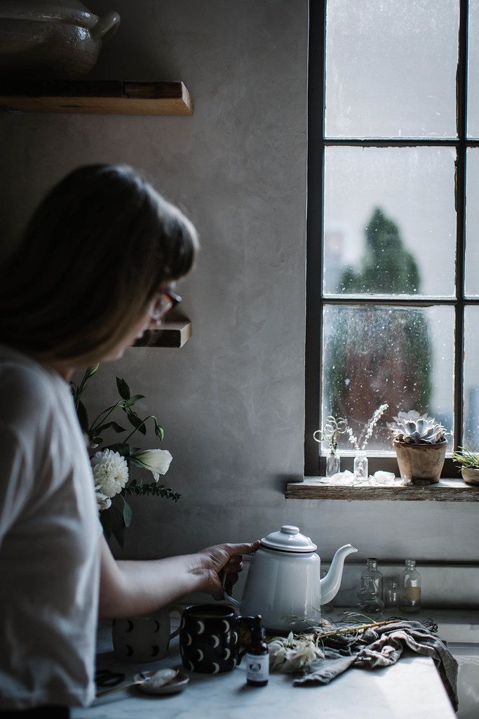 a woman sitting at a table in front of a window with flowers on the windowsill