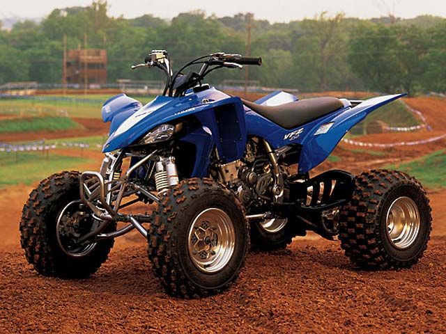 a blue four - wheeler is parked on the dirt in front of a baseball field