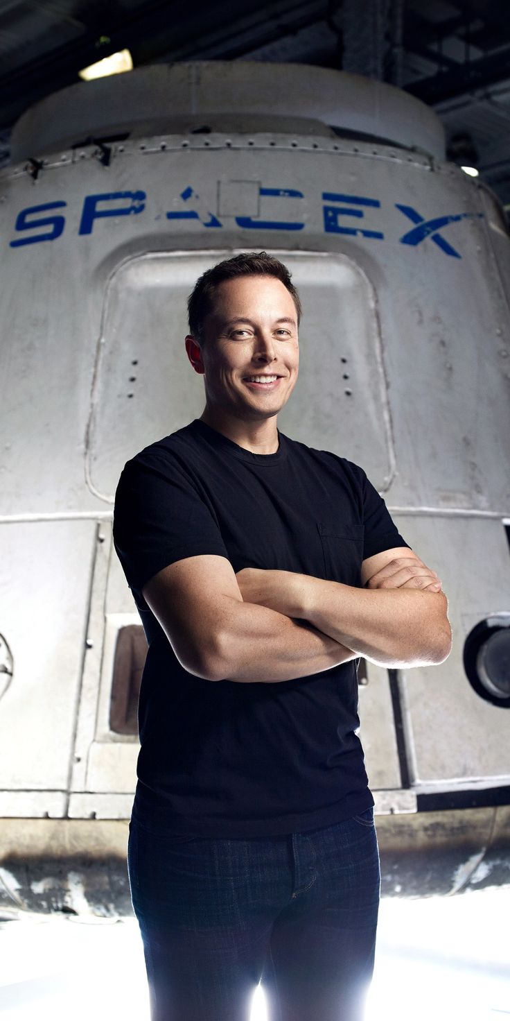 a man is standing in front of a spacex vehicle with his arms crossed and looking at the camera