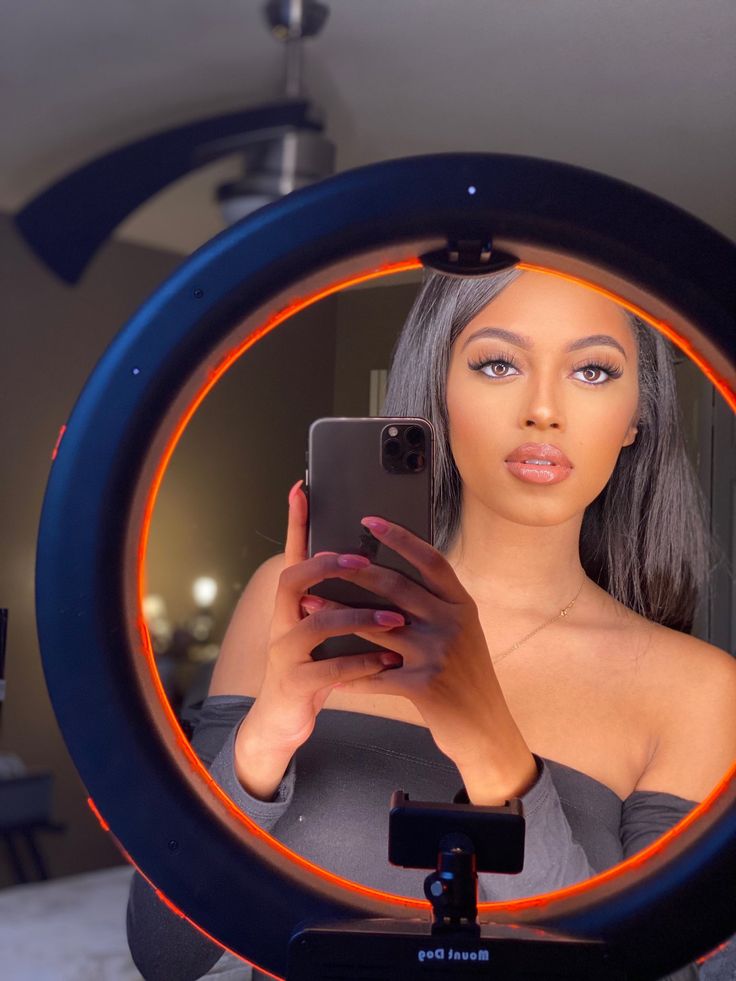 a woman is looking at her cell phone in the reflection of a round mirror with an orange ring around it