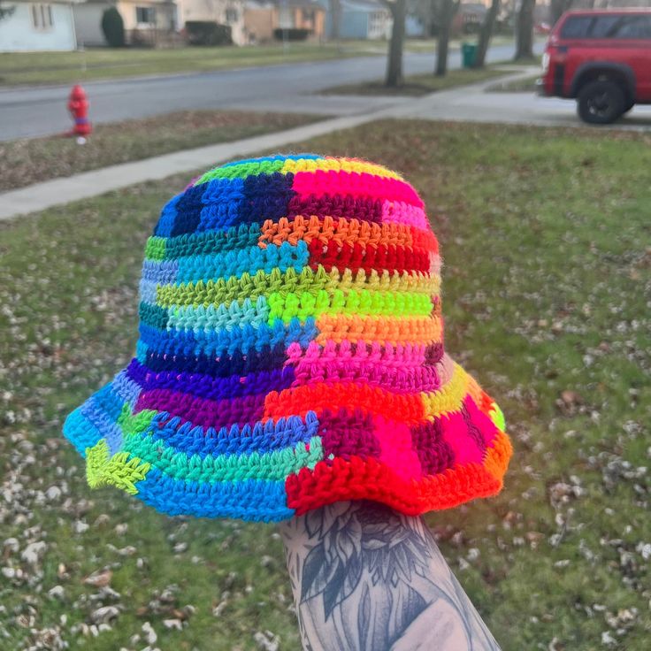 a person's hand wearing a multicolored crocheted hat on the grass