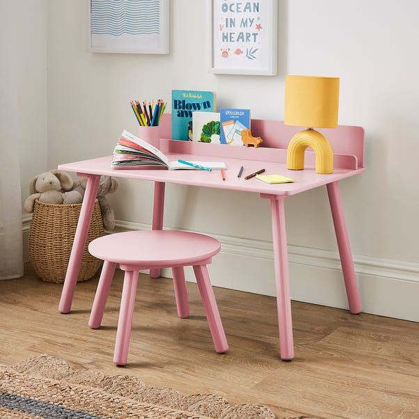 a child's pink desk and chair in a room with white walls, wooden flooring and artwork on the wall