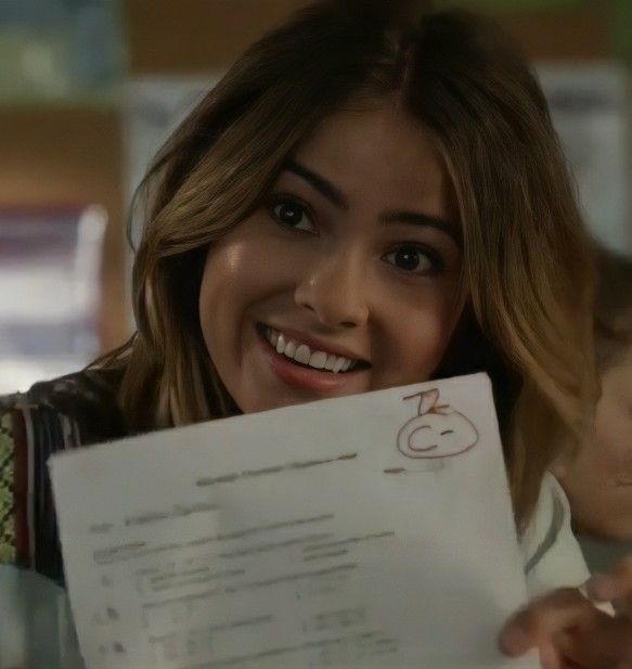 a woman holding up a piece of paper in front of her face and smiling at the camera