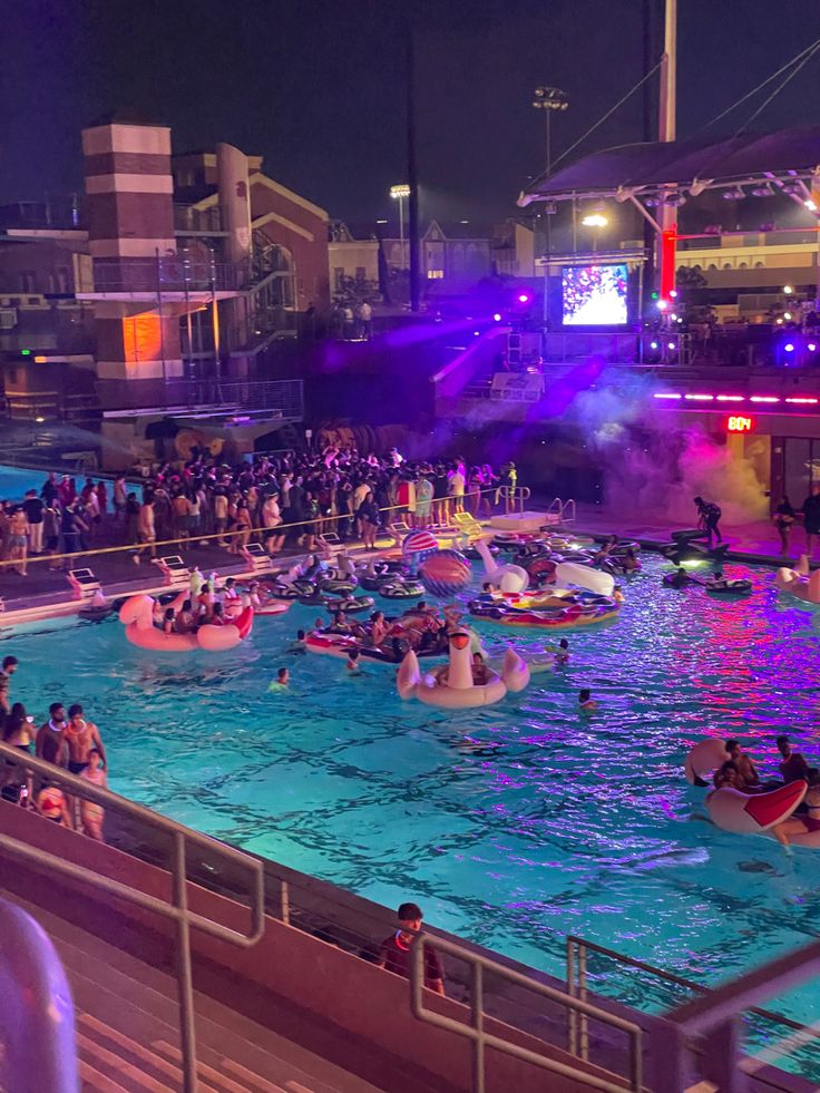 an outdoor swimming pool with many people in it and some onlookers watching