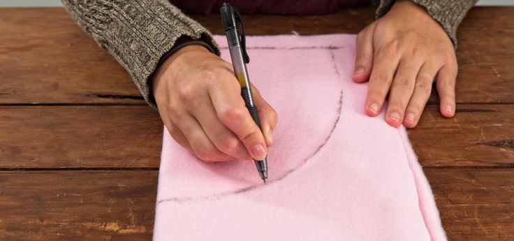 a woman is making a pink piece of fabric with a pen and thread on it