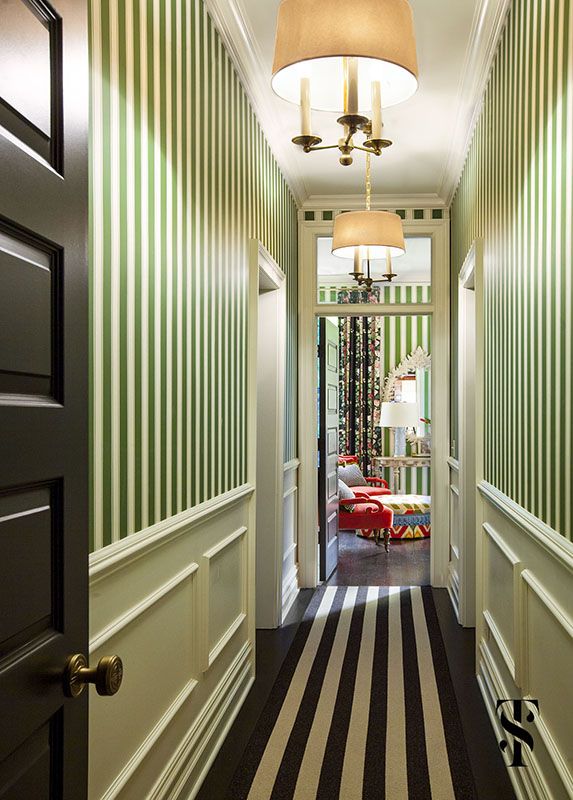 a hallway with green and white striped wallpaper, black door handles and two lamps hanging from the ceiling