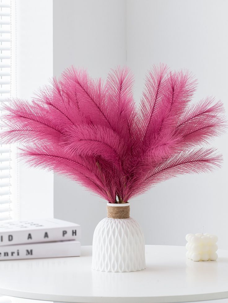 pink feathers in a white vase on a table