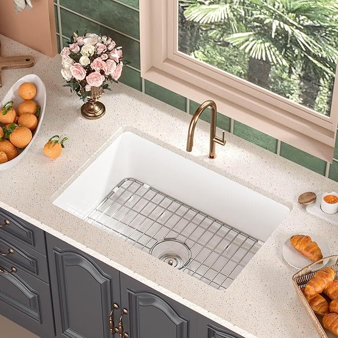 a kitchen sink sitting under a window next to a bowl of oranges and croissants