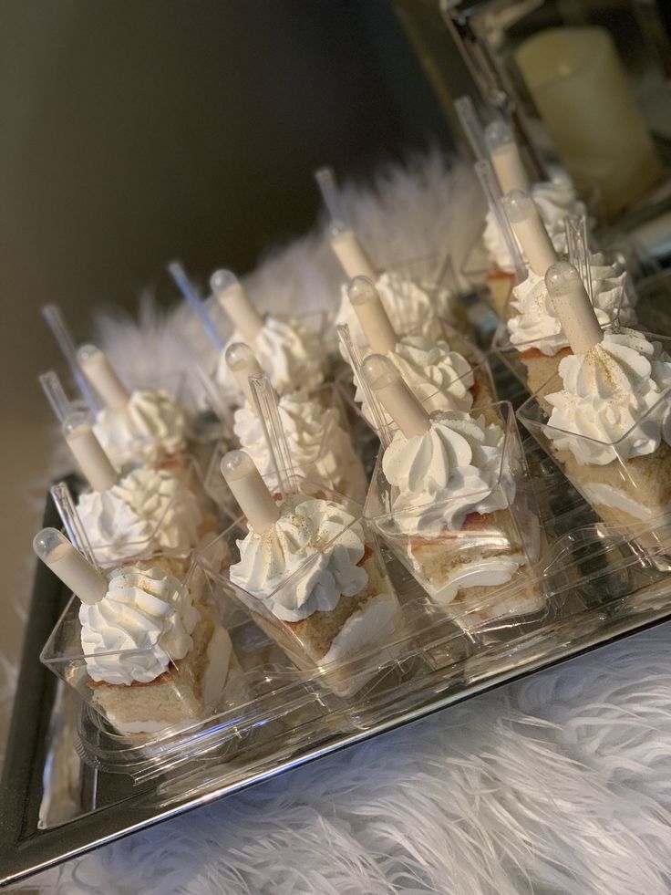 cupcakes with white frosting and candles are arranged in a row on a clear tray