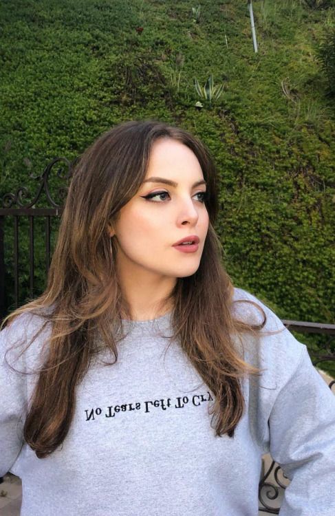 a woman with long brown hair wearing a grey sweatshirt and looking off into the distance