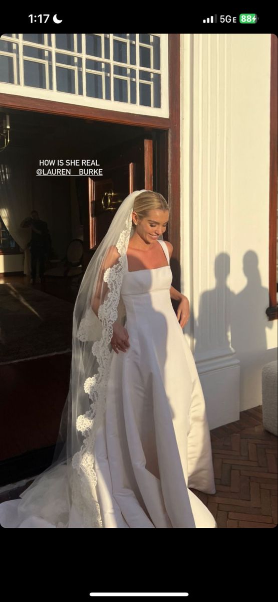 a woman in a white wedding gown and veil walking out of a building with her shadow on the ground