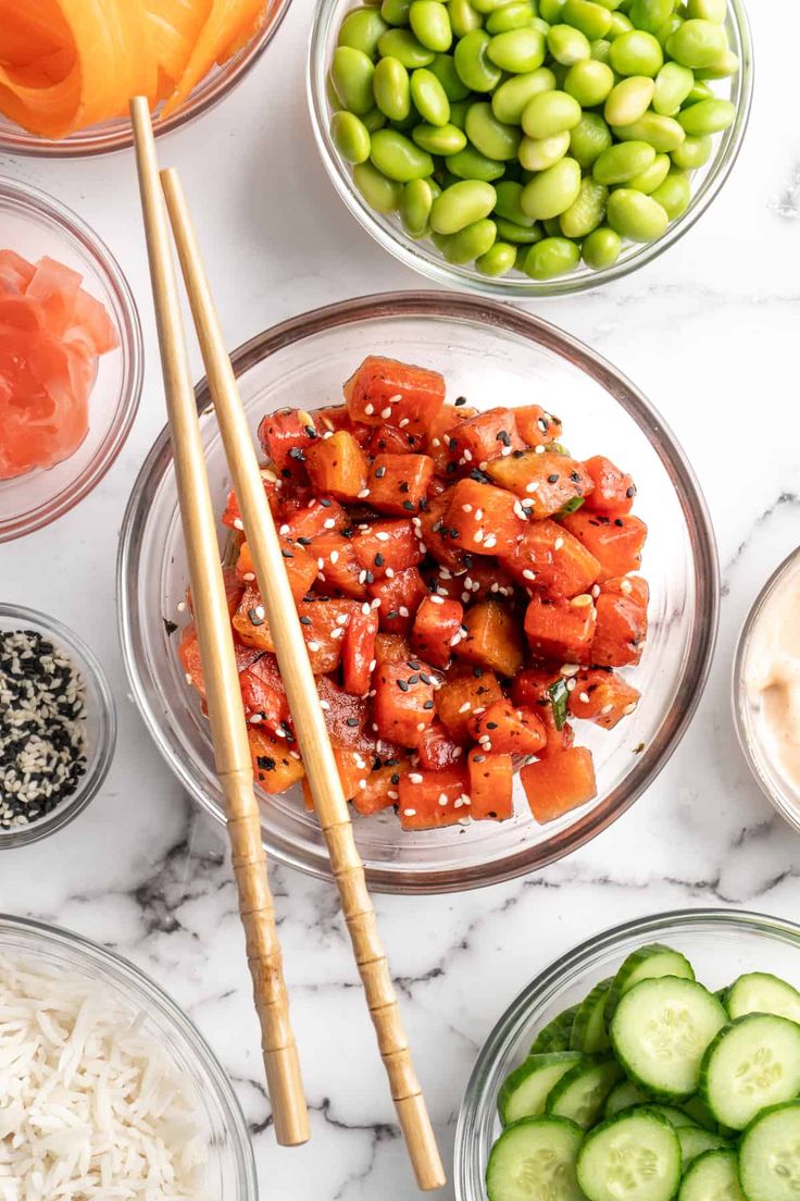 bowls filled with vegetables and chopsticks on top of a marble countertop next to sliced cucumbers