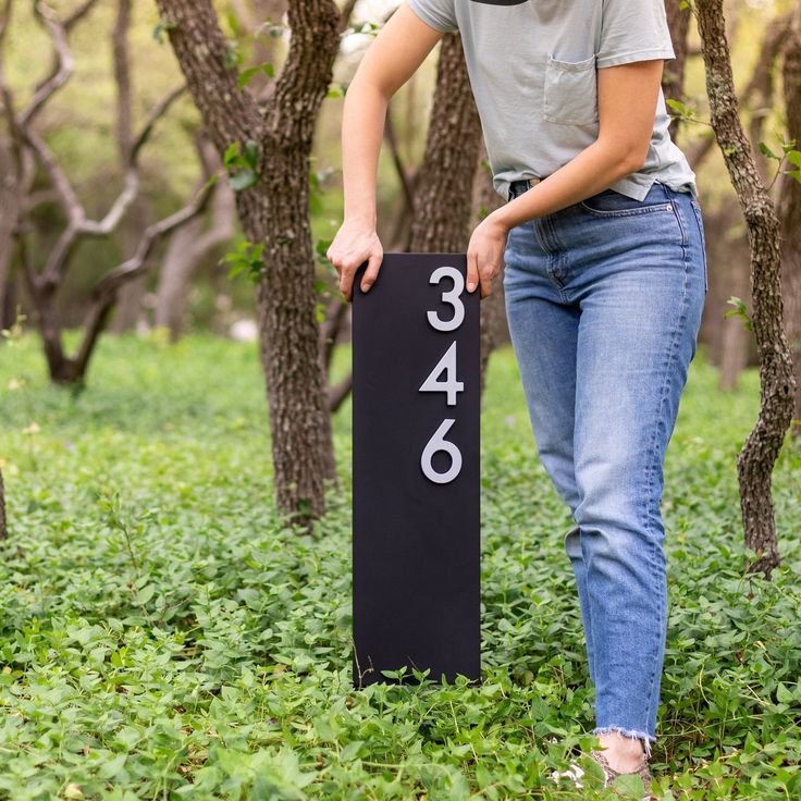 a woman standing next to a black sign in the grass with numbers printed on it