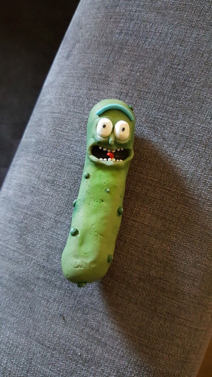 a green toy with googly eyes and mouth sitting on top of a gray couch